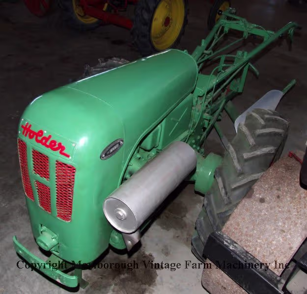 A small green Holder garden tractor with a two-way plough.